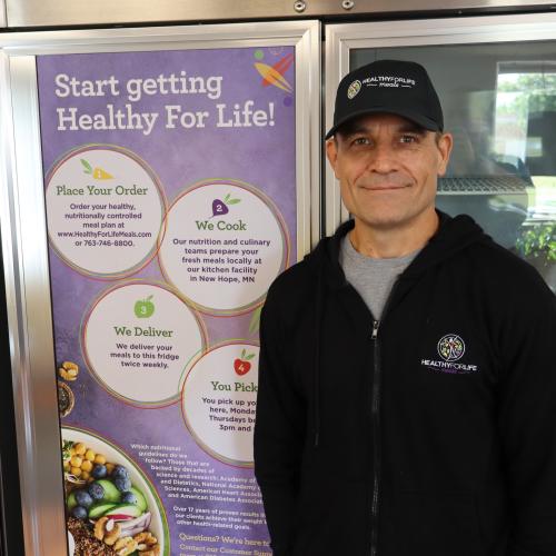 A man in a baseball cap stands next to a freezer