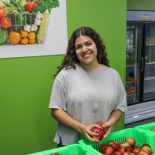 Young woman in gray t-shirt smiling at the camera, holding apples