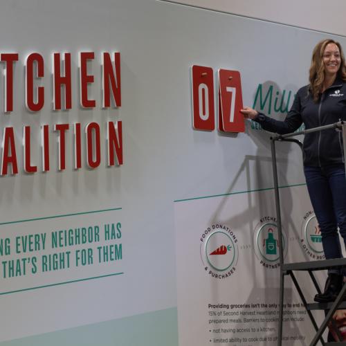 Woman on ladder smiles while hanging up number 7 on Kitchen Coalition mural.