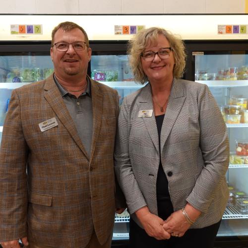 Two people wearing blazers and name tags standing in front of a cooler