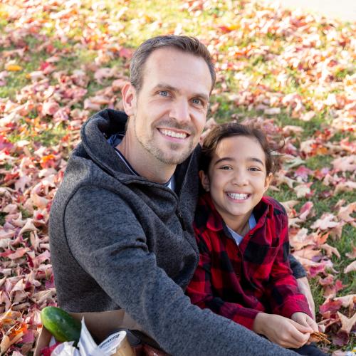 2 people pictured sitting outside on grass covered with autumn leaves - one adult one child