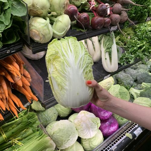 A hand picks out a napa cabbage from a grocery store