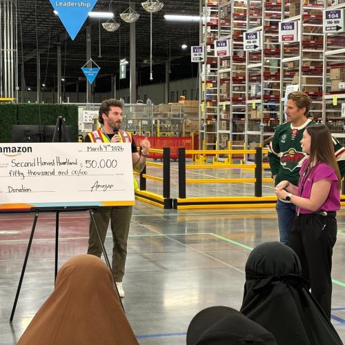 A large check is displayed by a person talking to a crowd in a warehouse