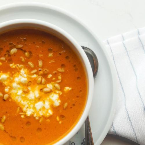 Orange soup with cheese on top in a white bowl with a plate, spoon and napkin