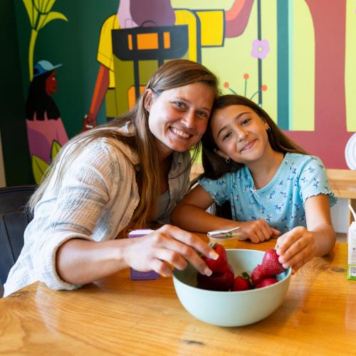 Adult woman with a child sitting at a table eating strawberries out of a bowl
