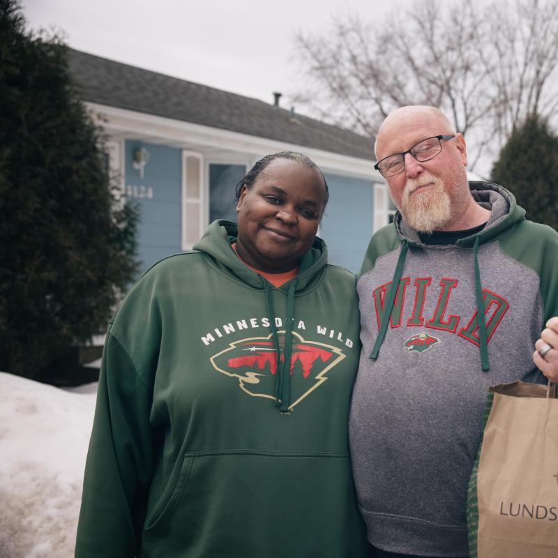 Two people standing outside, smiling and holding a grocery bag