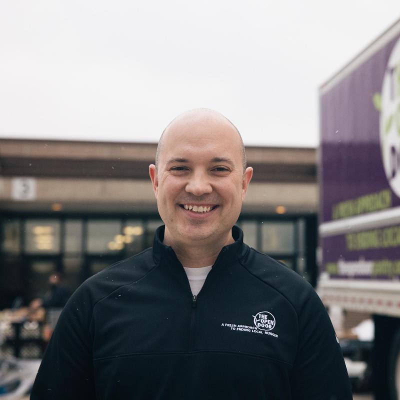 Closeup of a man standing outside smiling, next to a semi truck