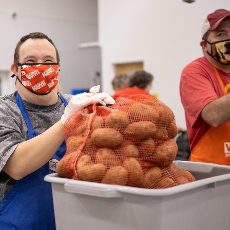 A volunteer smiles while holding a bag of sweet potatoes