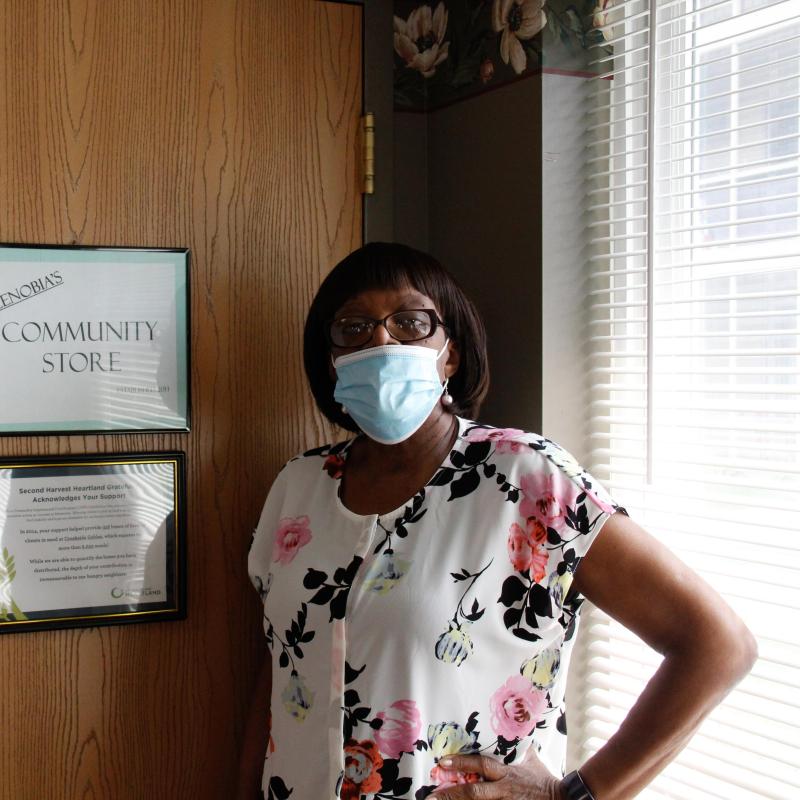 A woman stands in front of a sign that says, "Zenobia's Community Store"