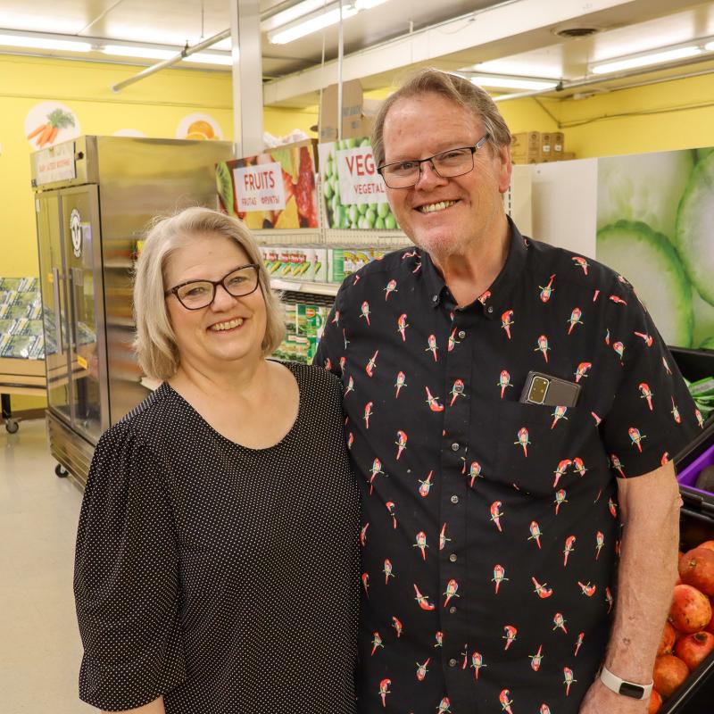A man and woman posing in glasses and black shirts in a food shelf