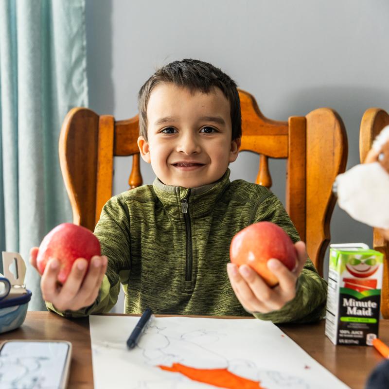 child sitting at table with fruit in both hands