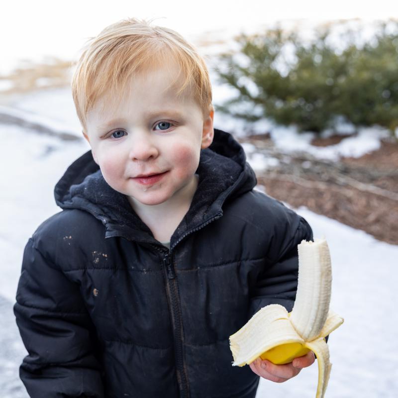 child outside in winter weather holding banana