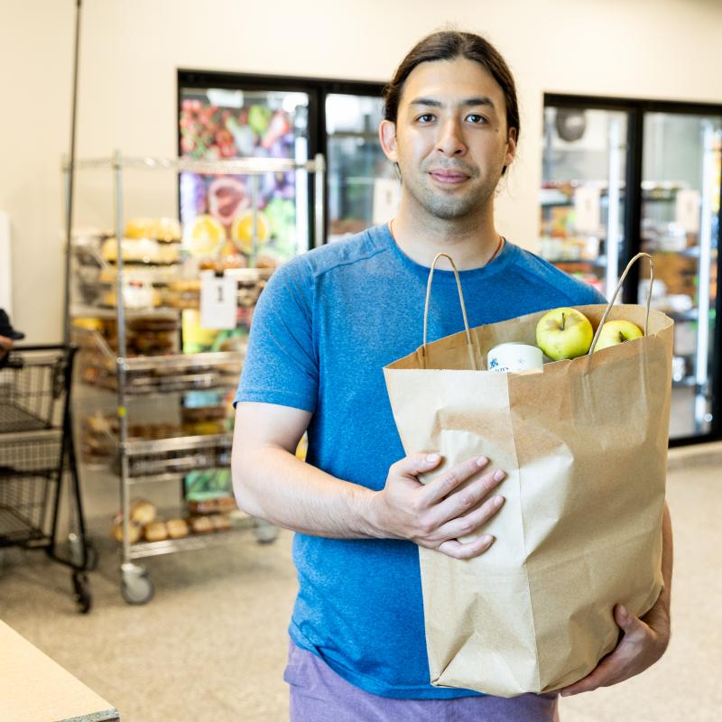 Man standing in food shelf with paper bag of grocery items