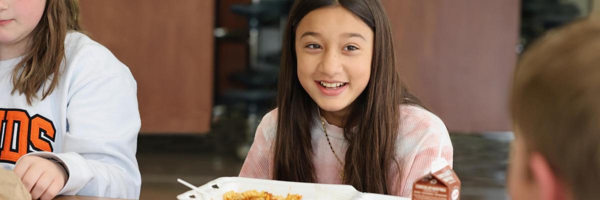 Young girl eats lunch with friends at school