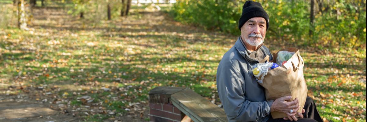 Man sits on a picnic table with a bag of groceries