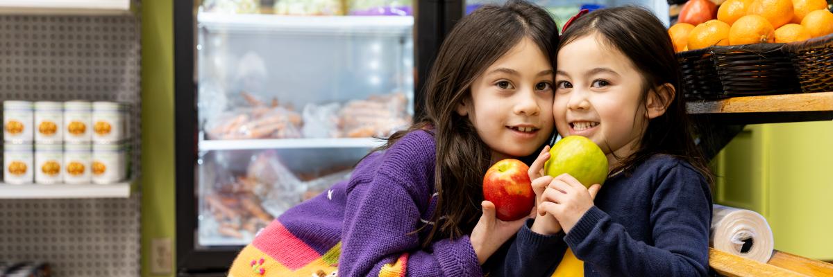 Two Children holding apples in front of refridgerator display