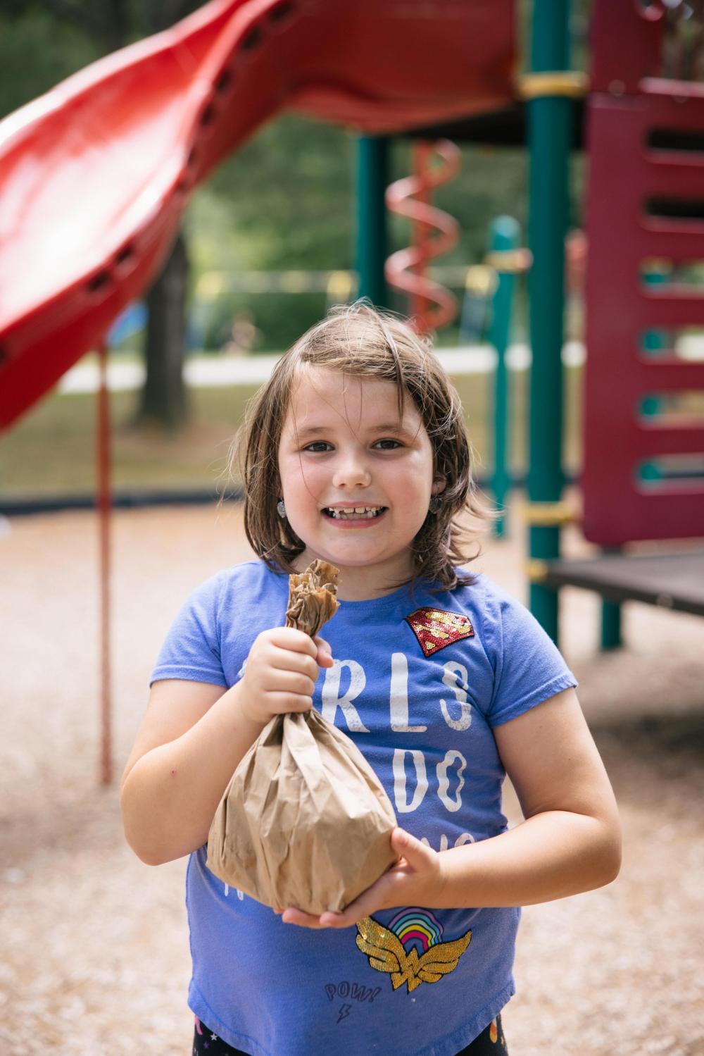 Scarlet holds a summer meal A young girl holds a brown paper bag while smiling at the camera