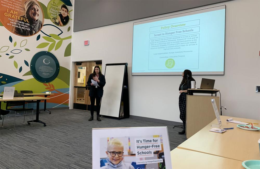 Rachel Sosnowchik and Maren Guptill from the Public Affairs Team present at the advocacy training session held at Second Harvest Heartland. The presentation shows a policy overview to “Invest in Hunger Free Schools.” A postcard on the table reads “It’s Time for Hunger-Free Schools.”