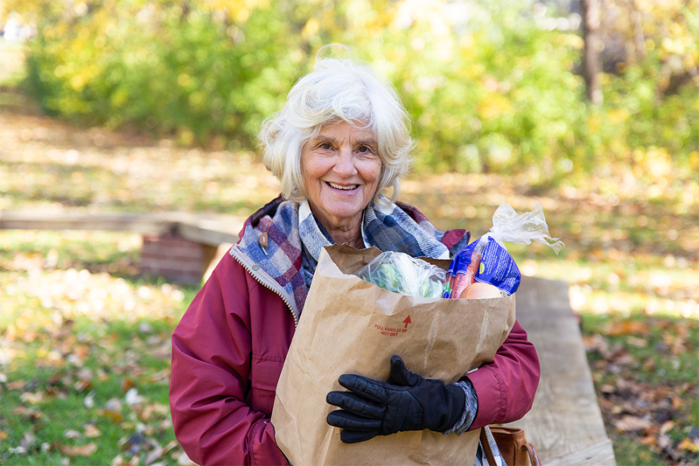 Woman smiling and standing with a grocery bag.