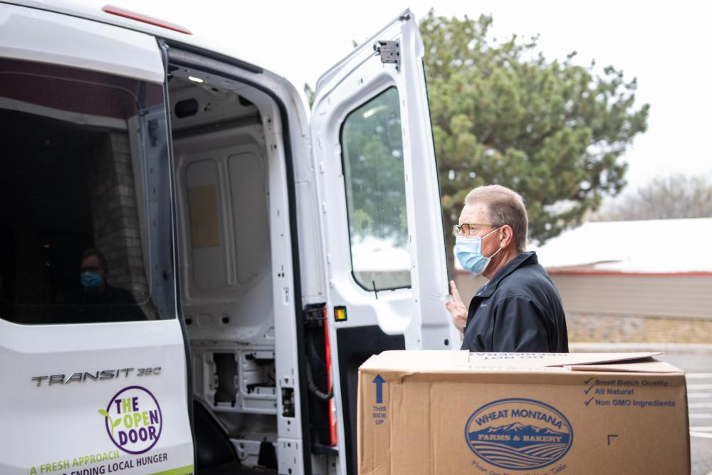 A man holds open the back door of a truck next to a box of food