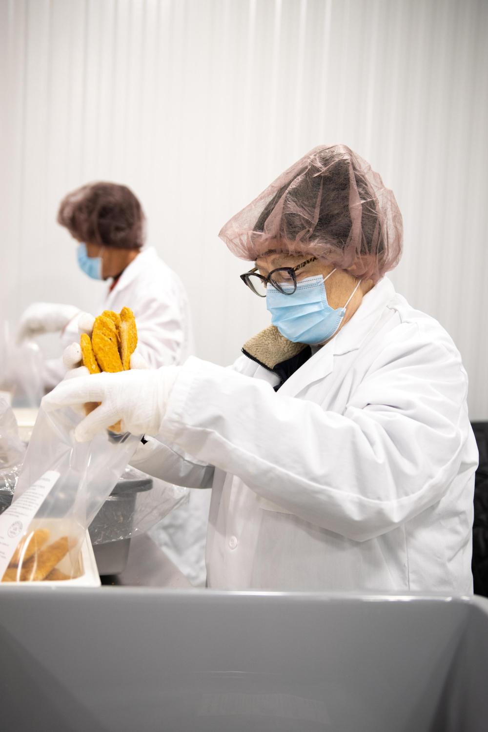A volunteer wearing a hair net and coat packs frozen chicken in a plastic bag 