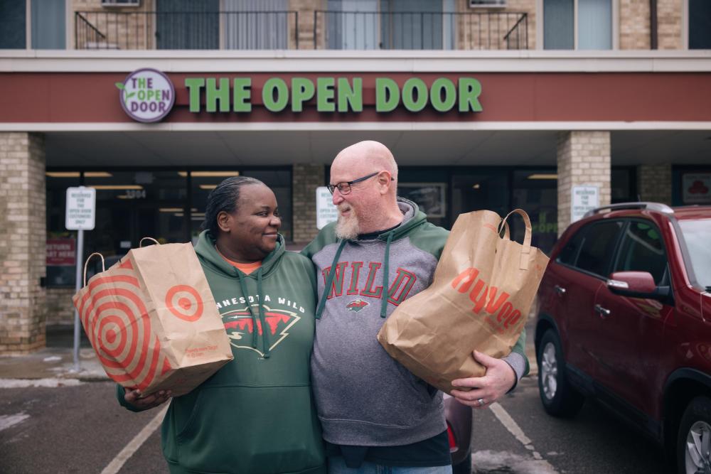 A couple looks at each other and smiles while holding bags of groceries