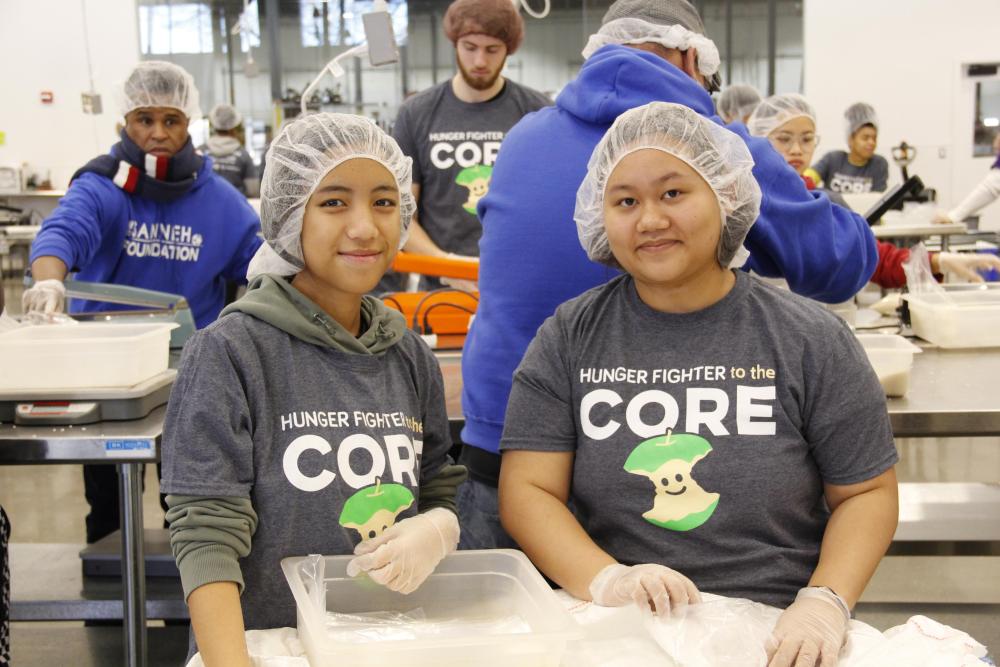 Two people smile at the camera while wearing hair nets in the Volunteer Center