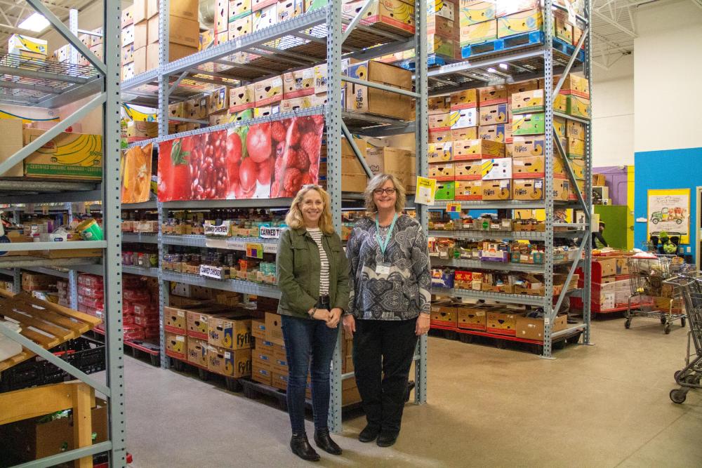 Two women stand in front of shelves of boxes