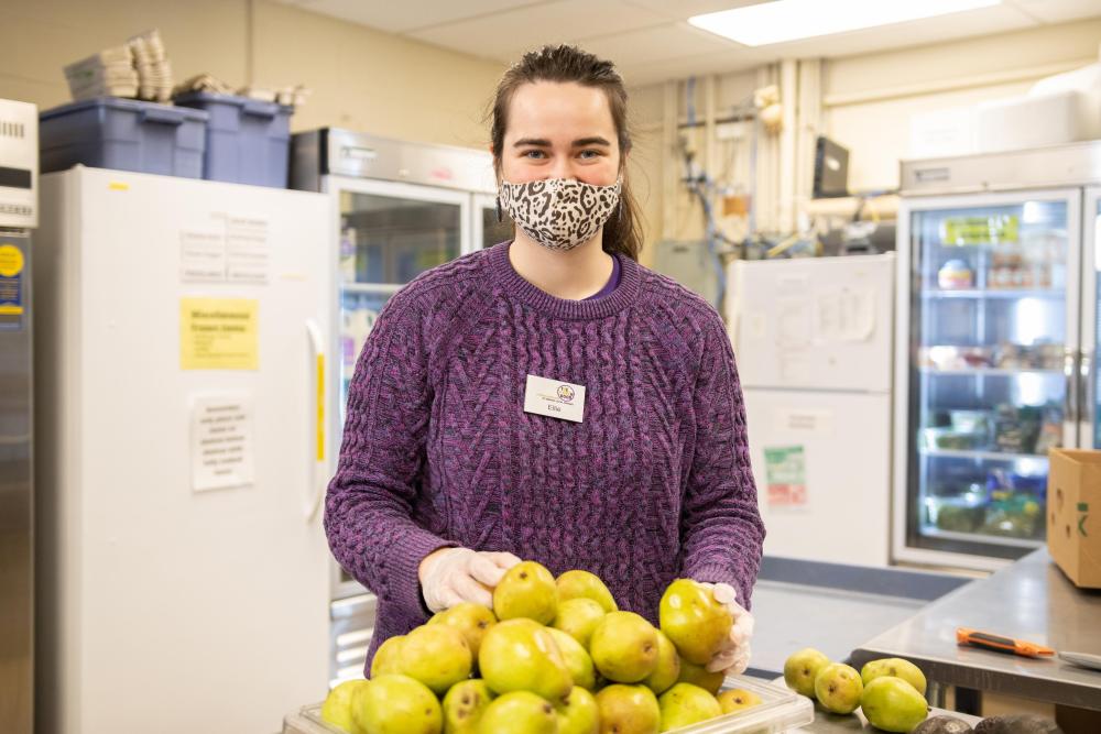 A woman smiles at the camera holding a pear