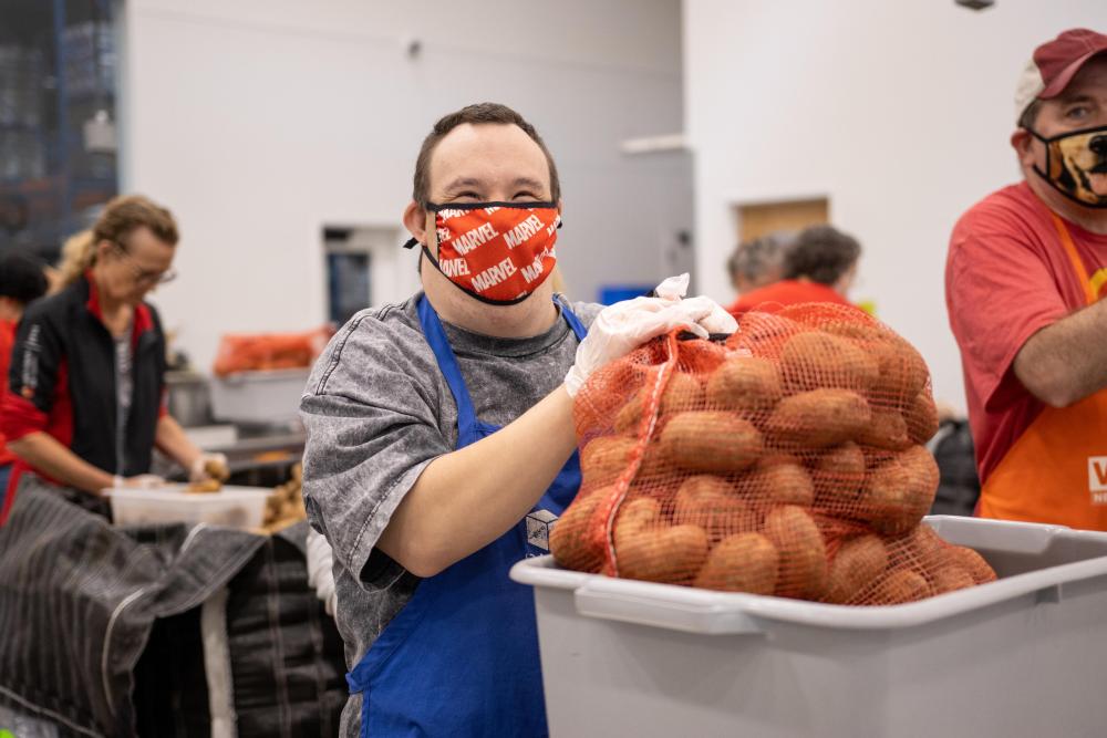 A volunteer smiles while holding a bag of sweet potatoes