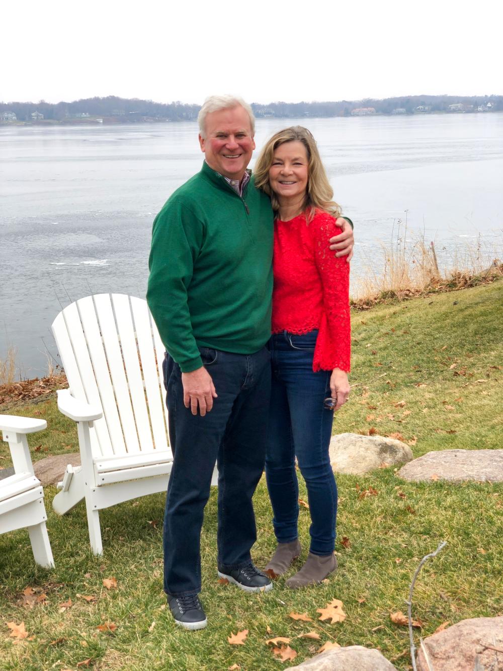 Two people stand together in front of a lake