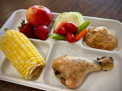 Chicken, corn, fruit and cookie on a lunch tray