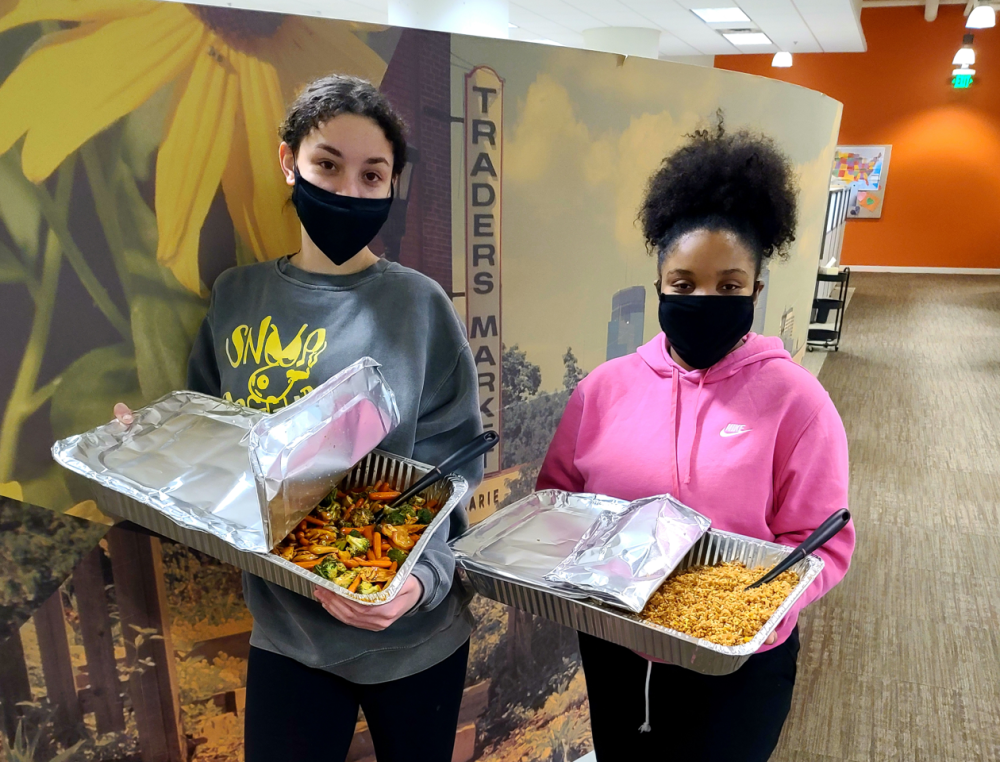 Two young girls hold pans for prepared meals for their class