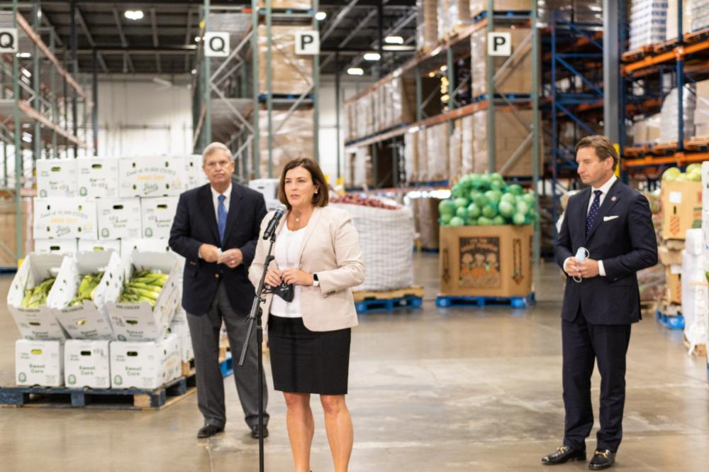 Leaders in agriculture and politics stand in a food bank warehouse speaking to media