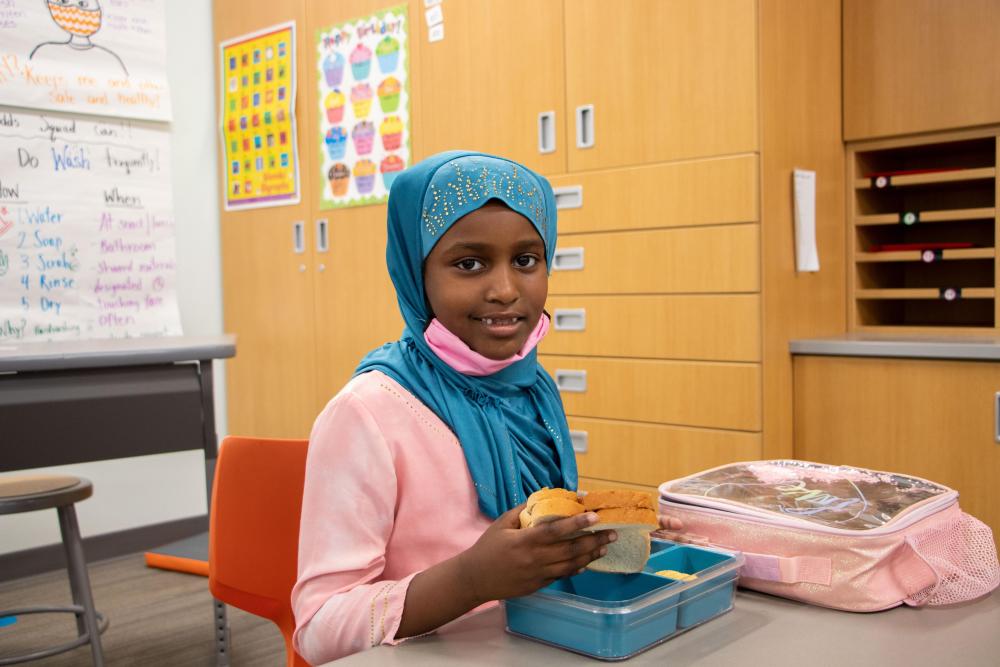 Young child in head scarf eating lunch at school