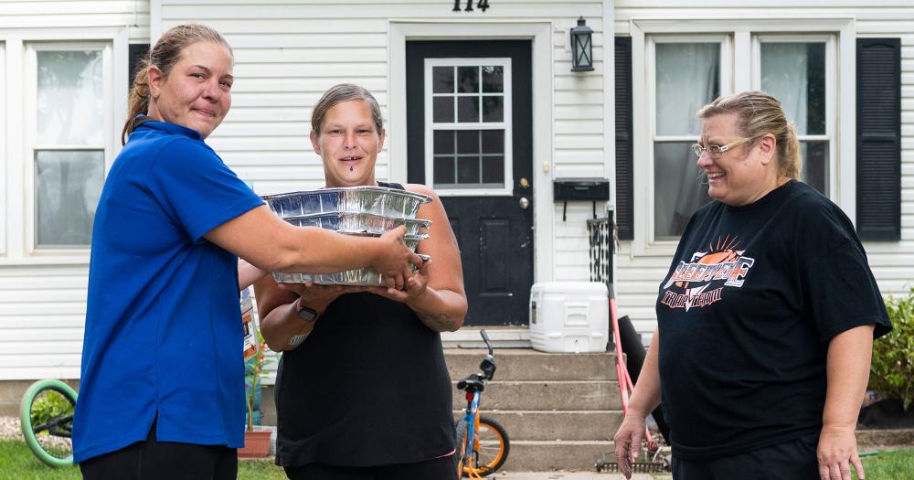 hunger in Minnesota three women standing outside their home holding containers of prepared food