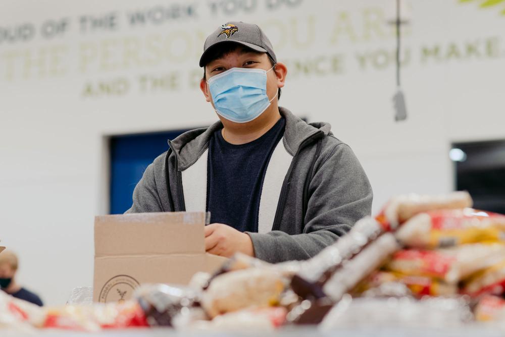 A volunteer smiles at the camera while packing a FOODRx box