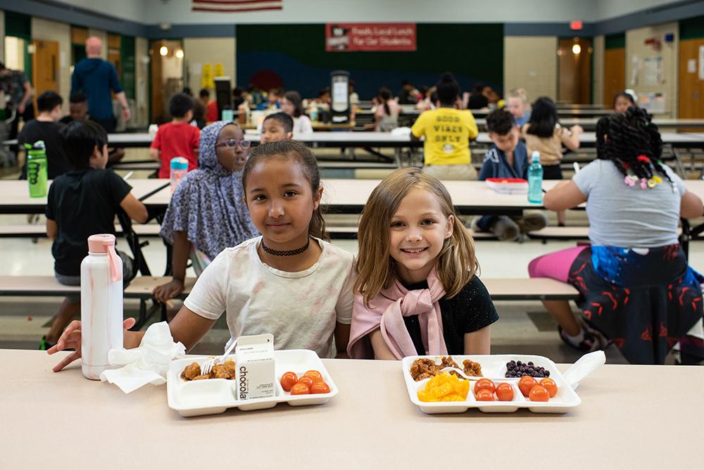 Two young girls sitting at a cafeteria lunch table