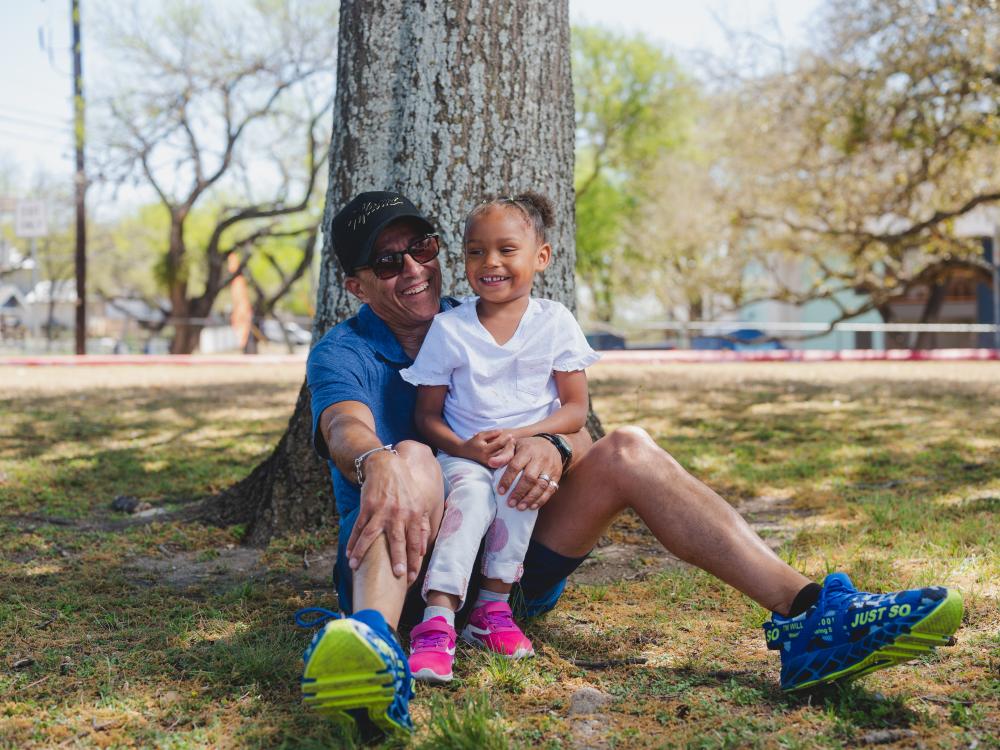 Dad sitting by tree with daughter in his lap, both smiling