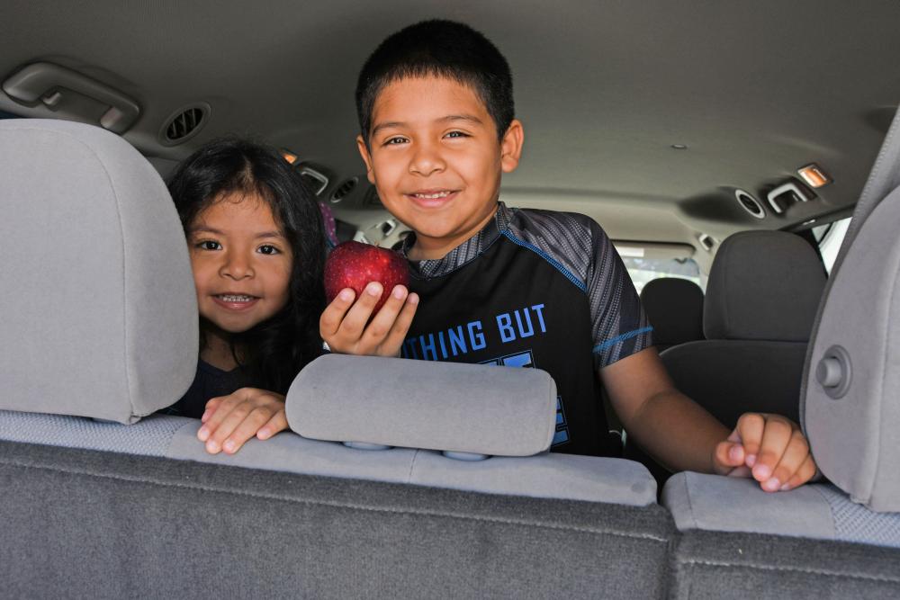 young girl and young boy smiling in a car, boy holding apple