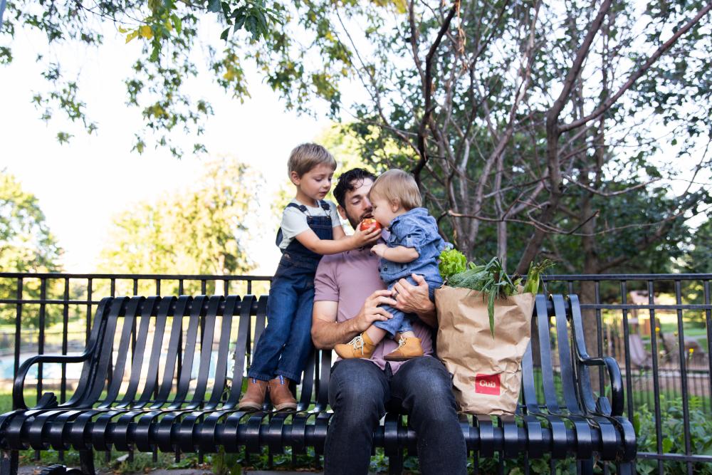 man and two kids on a park bench with an apple