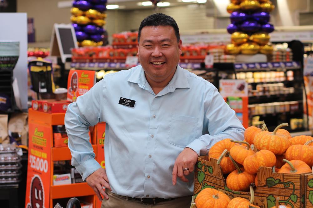 A grocer stands near a display of pumpkins