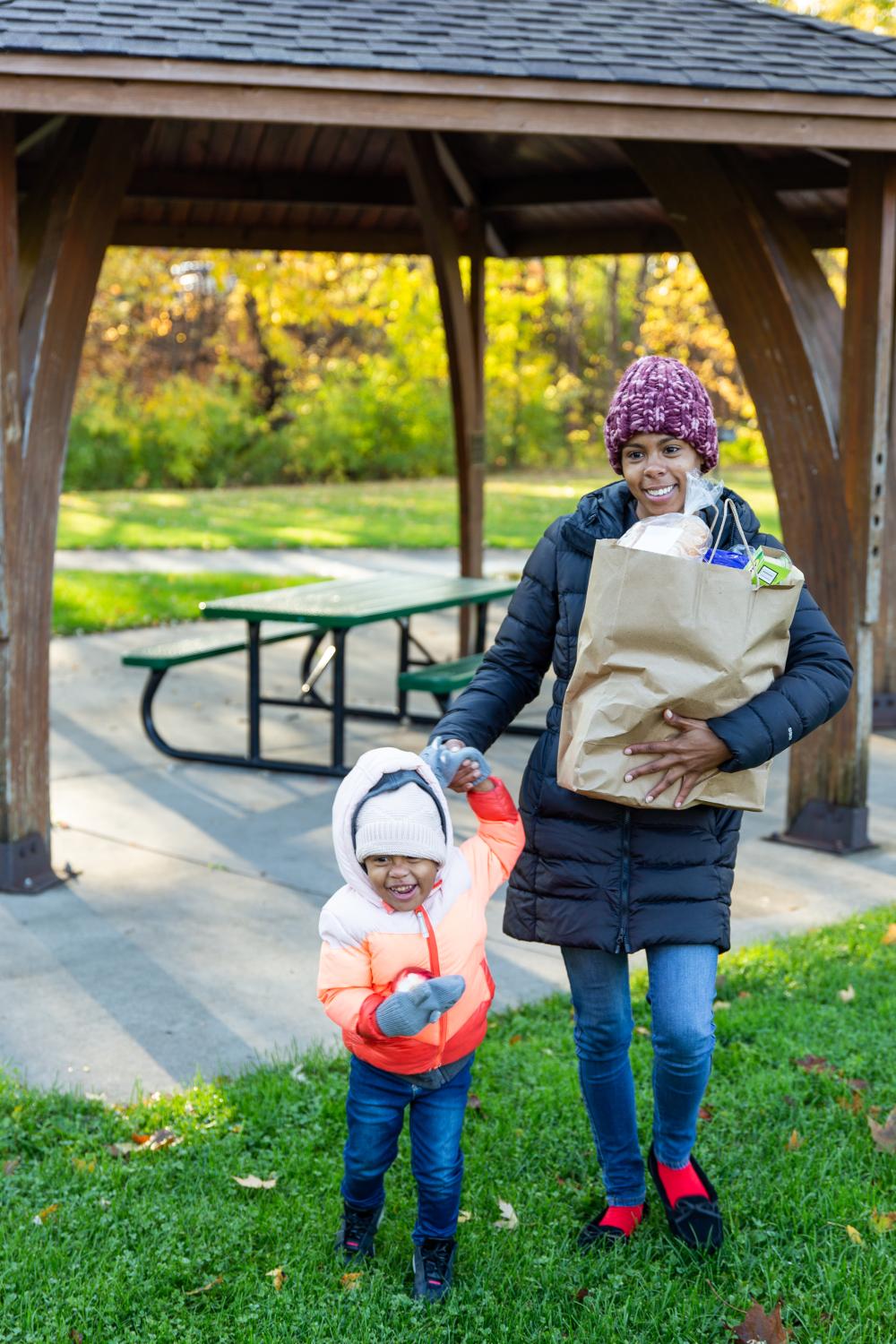 A mother and child walk through a park carrying groceries