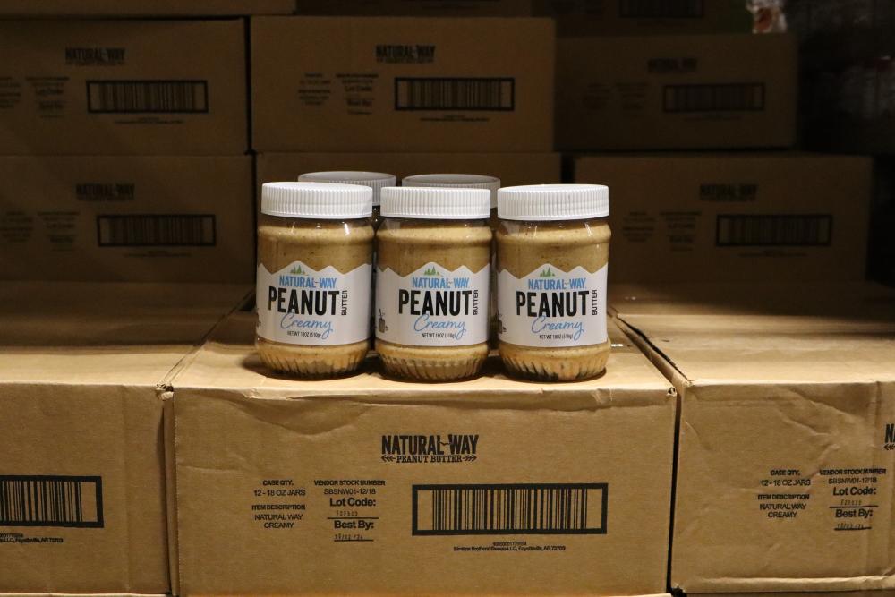 3 jars of  Natural Way creamy peanut butter on top of additional boxes of peanut butter