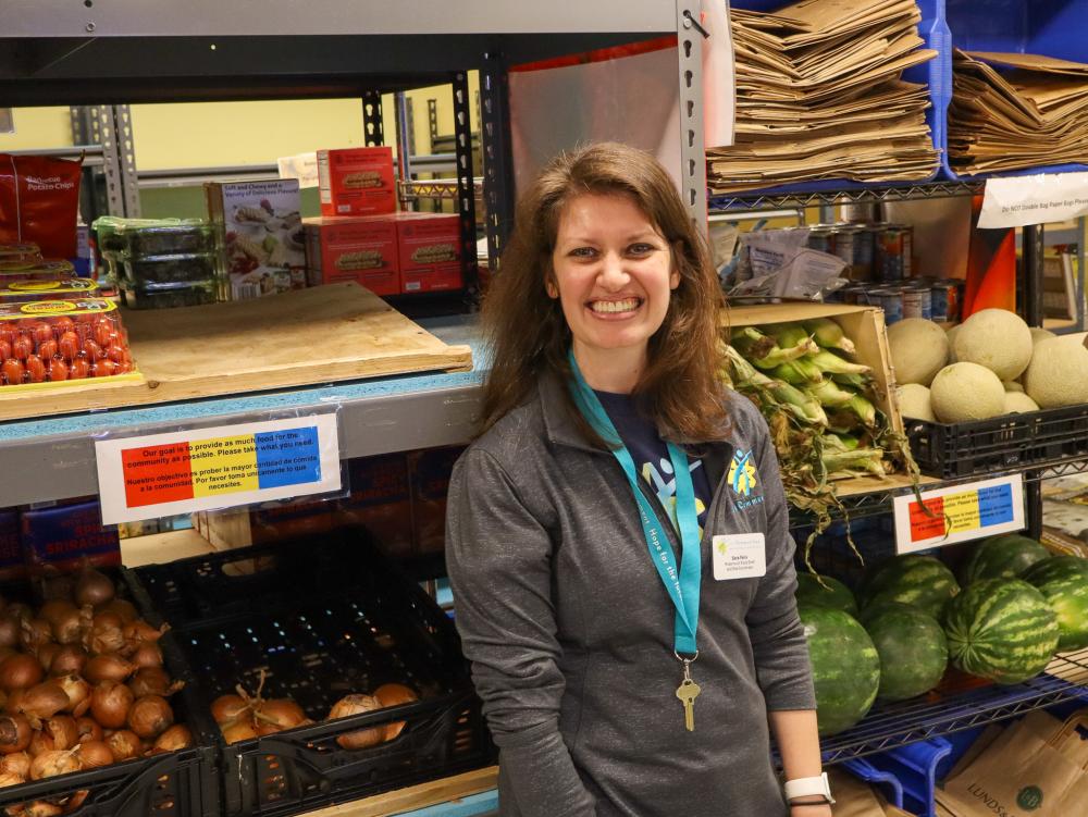 Sara Felix of 360 Communities Rosemount A brunet woman in gray smiling at the camera in front of shelves of food