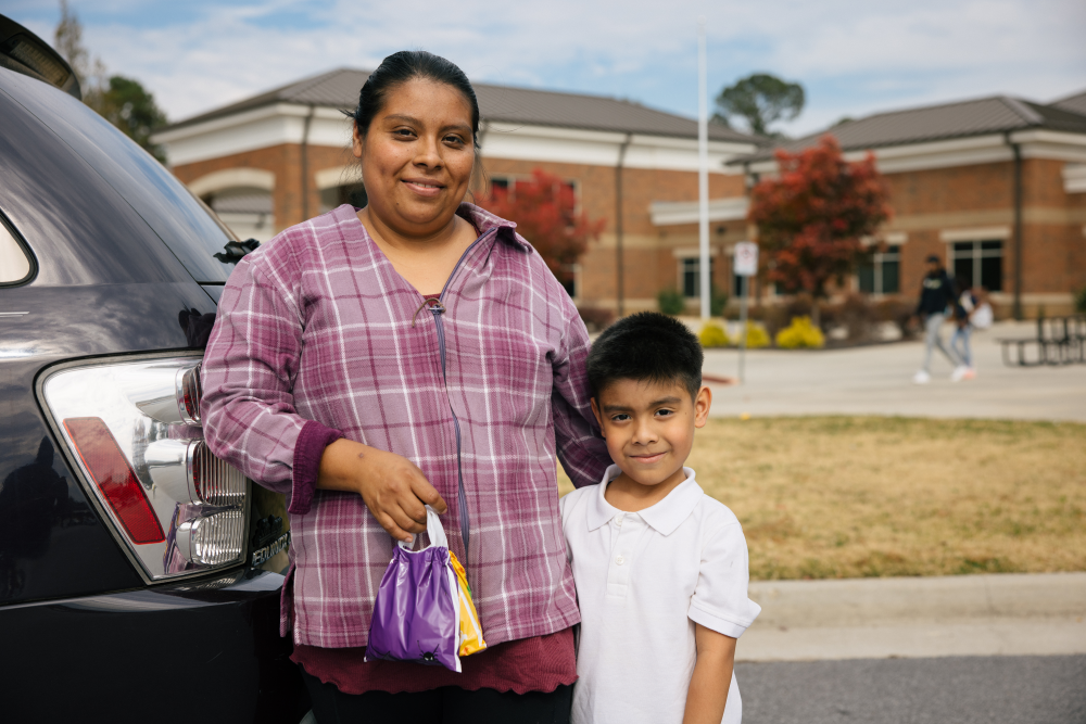 One adult holding a bag and one child standing in front of school - 