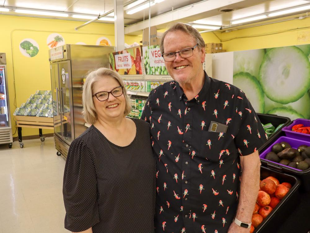 A man and woman posing in glasses and black shirts in a food shelf
