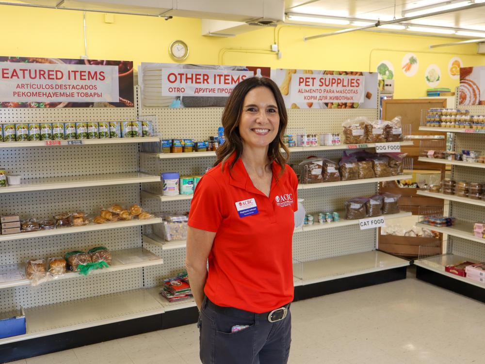 Stephanie Lehman, a brunette woman in a red shirt, stands in front of shelves of food