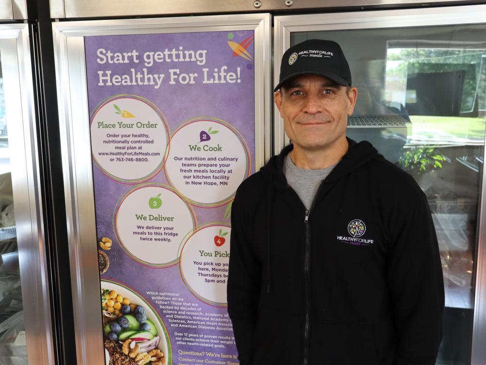 A man in a baseball cap stands next to a freezer