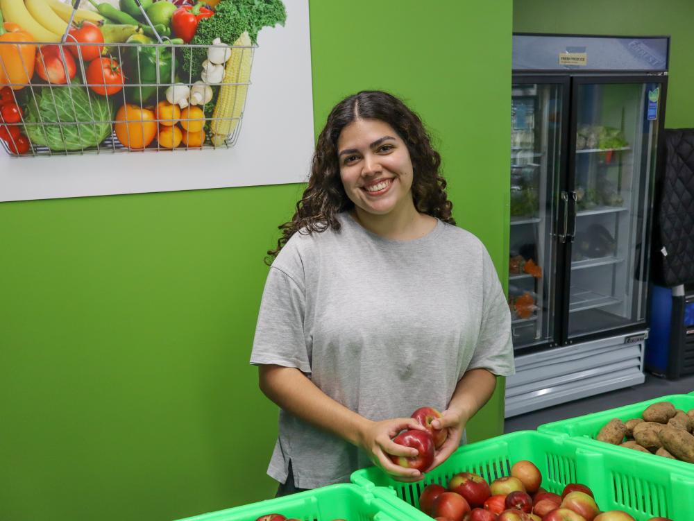 Young woman in gray t-shirt smiling at the camera, holding apples